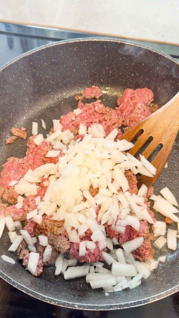 diced onions on top of raw ground beef in a skillet