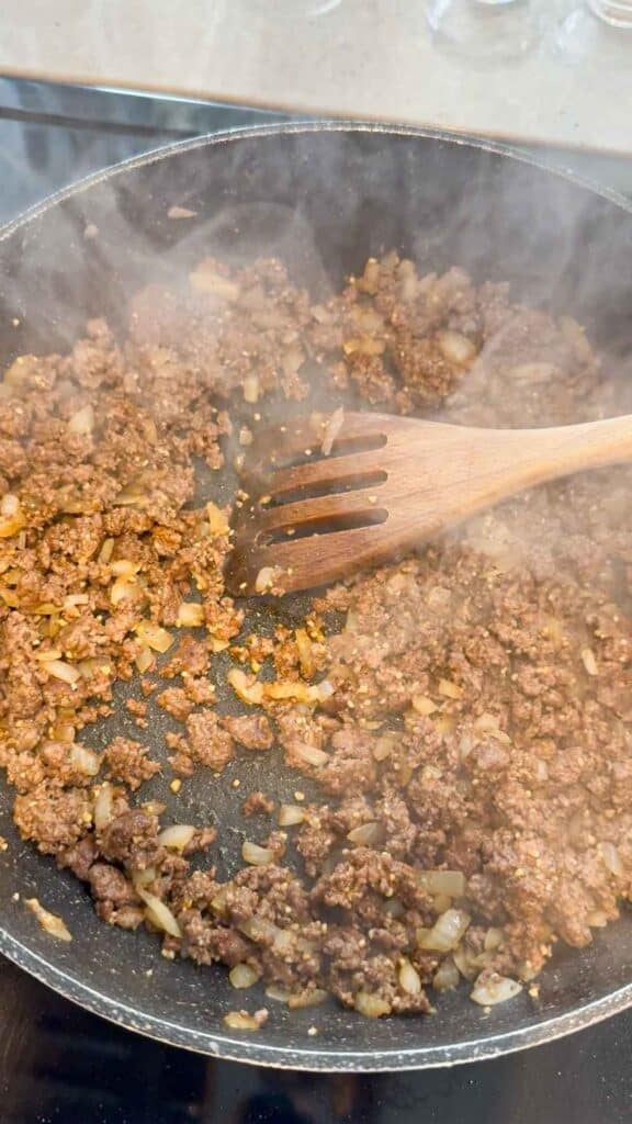 seasonings being stirred in to cooked ground beef in skillet