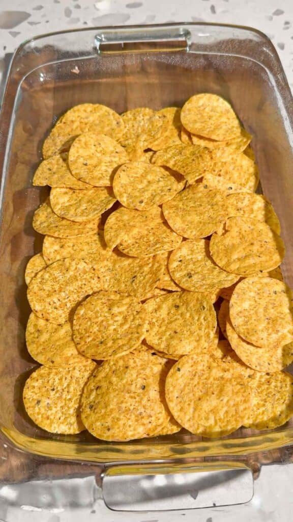 yellow corn tortilla chips in the bottom of a glass baking dish