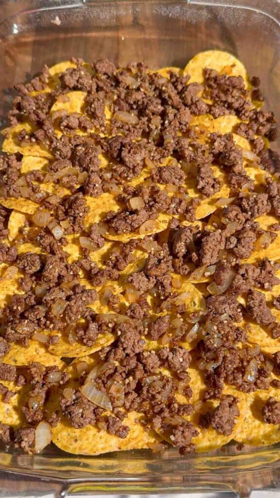 cooked ground beef on top of tortilla chips in a baking dish