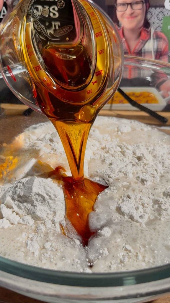 maple syrup being poured into pancake batter mixture