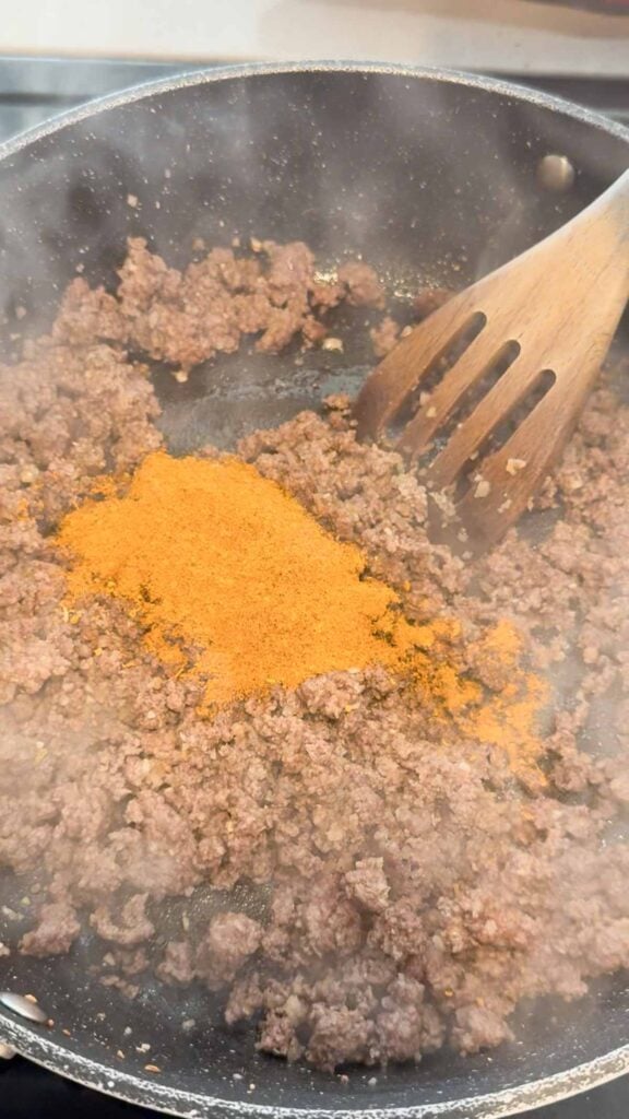 taco seasoning added to skillet with cooked ground beef