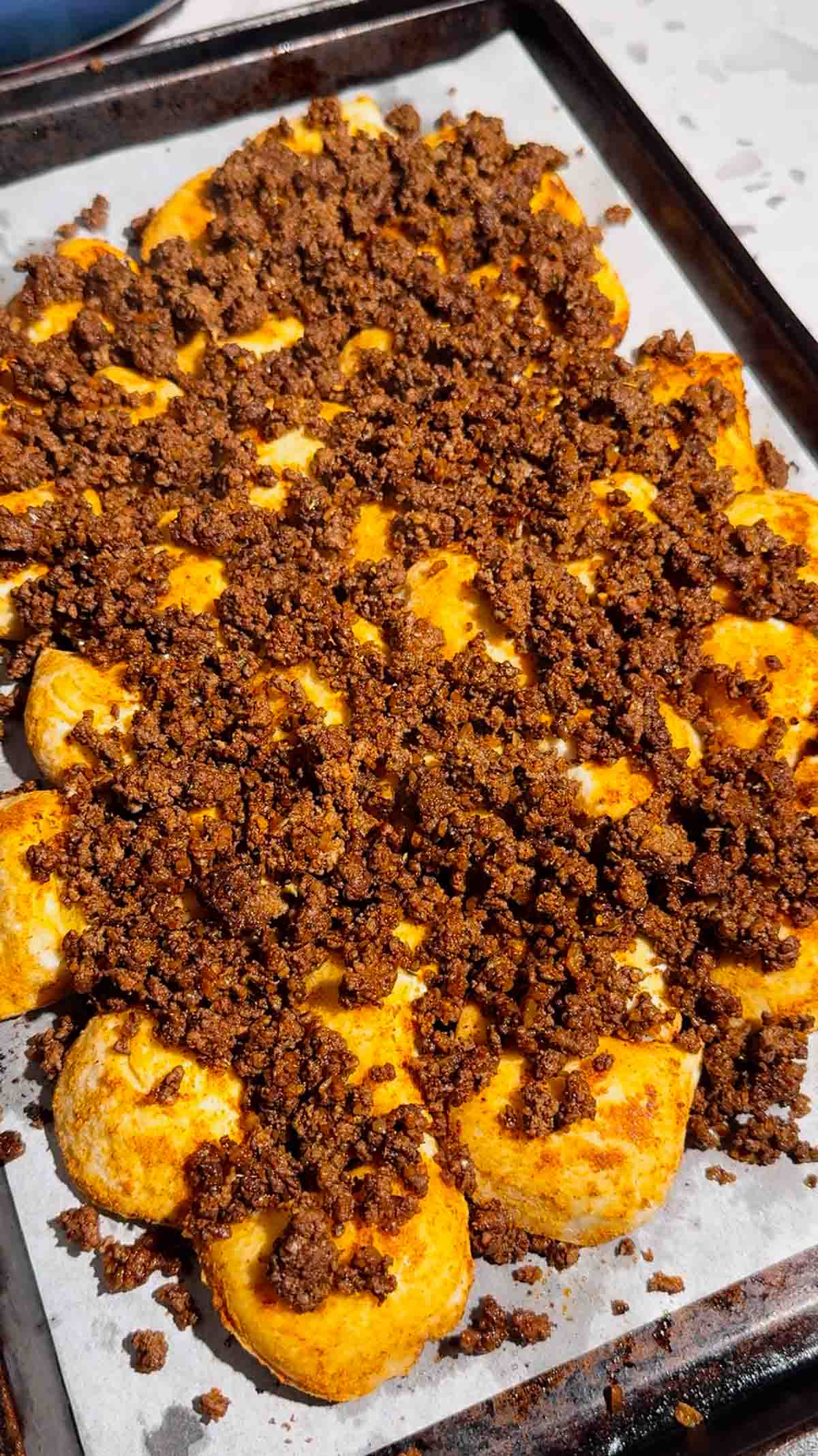 ground beef on top of crispy pierogies on a baking sheet