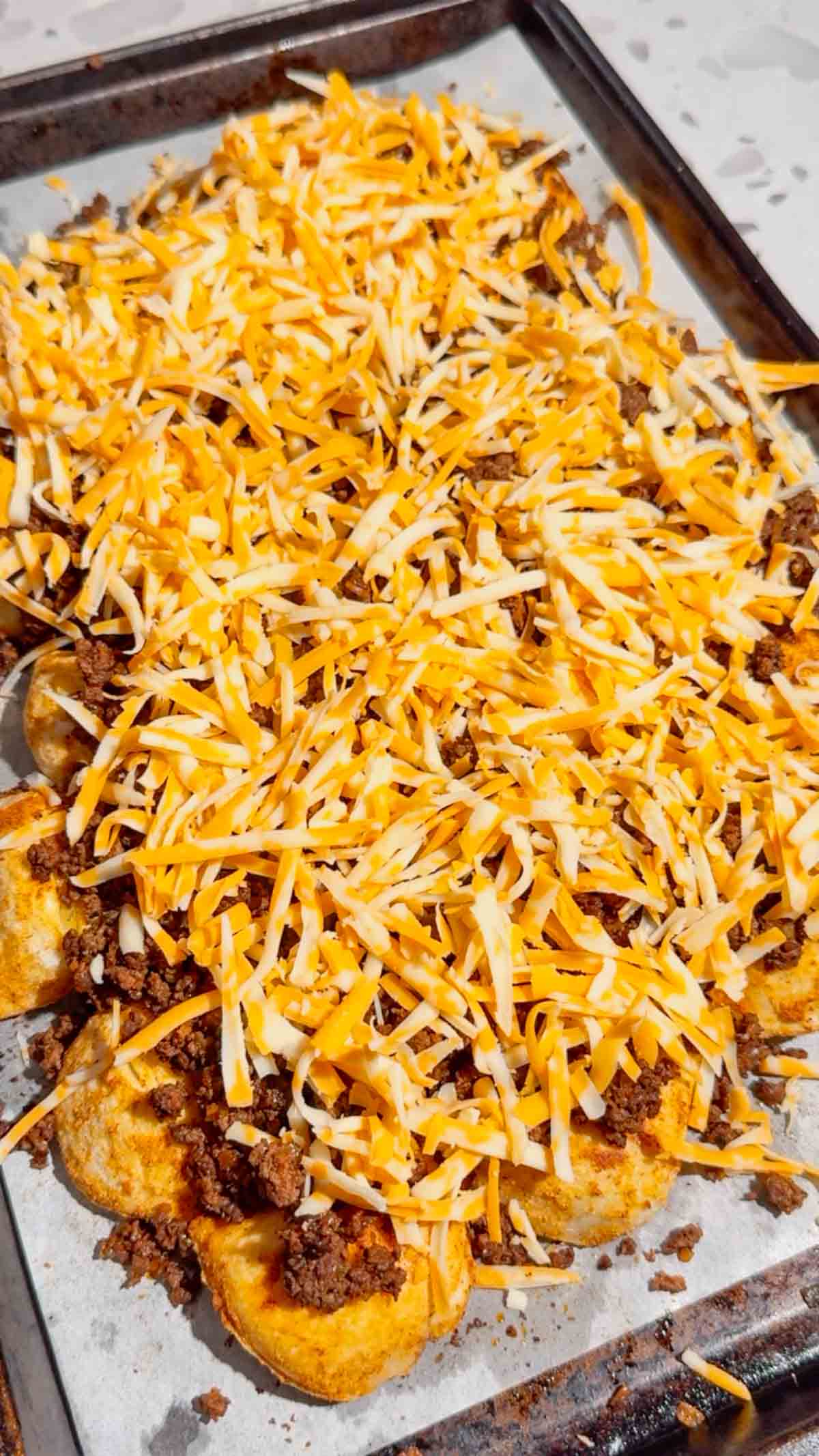 shredded cheddar on top of pierogi nachos on a baking sheet