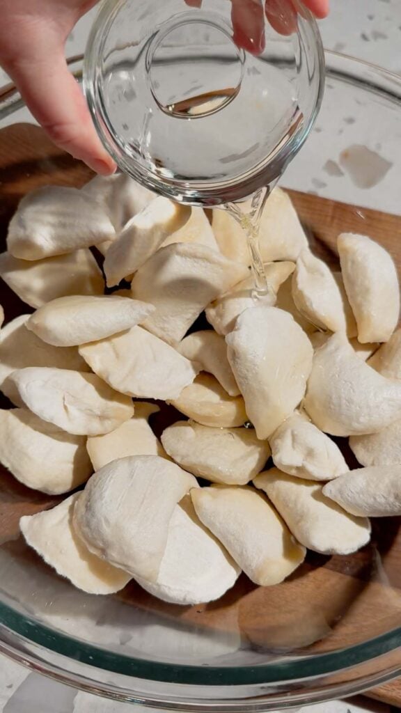 pouring oiil over frozen pierogies in a glass mixing bowl