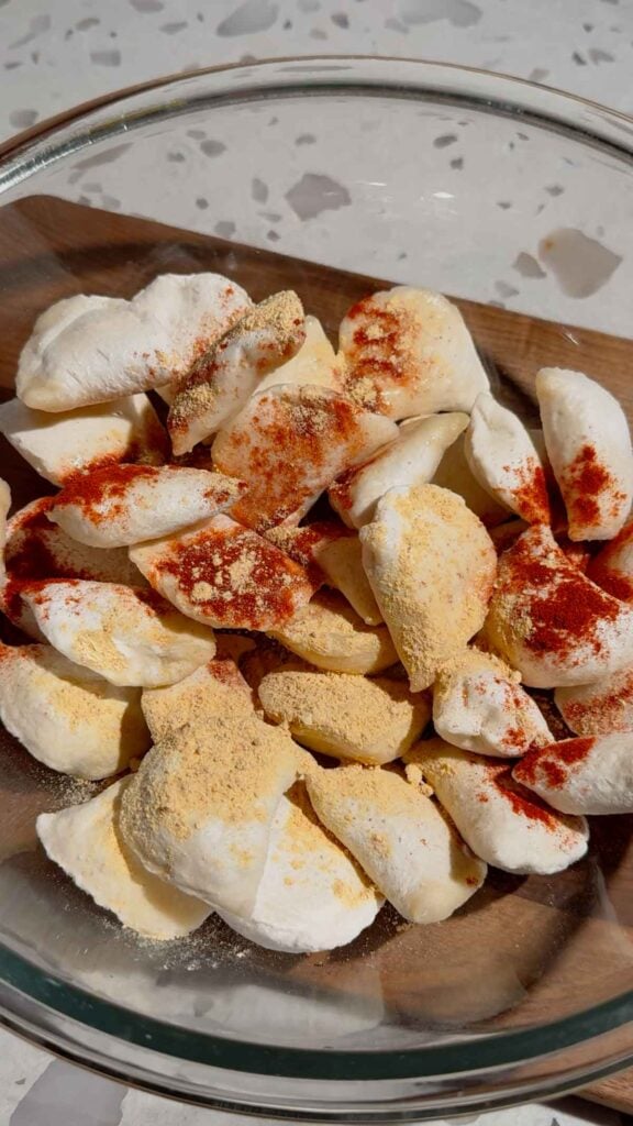 garlic powder, onion powder and smoked paprika on top of frozen pierogies in a glass mixing bowl