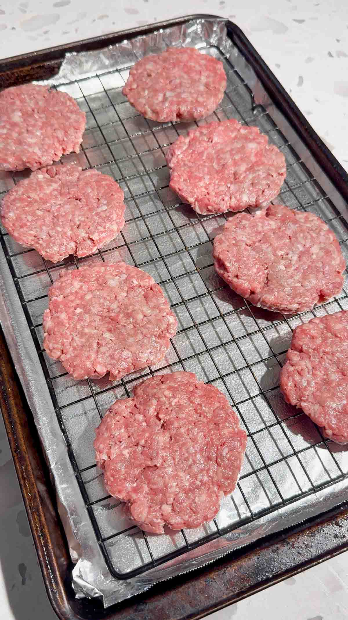 raw hamburger patties on a rack on a foil lined baking sheet