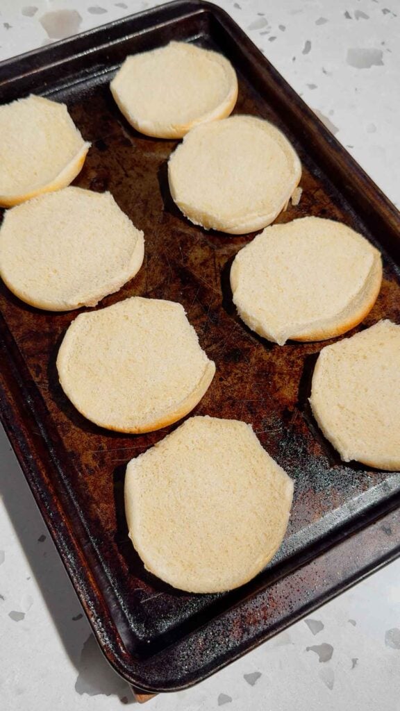 bottom halves of burger buns on a baking sheet