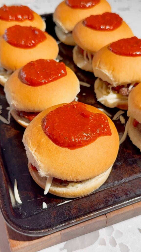 pizza sauce on top of hamburgers on a baking sheet