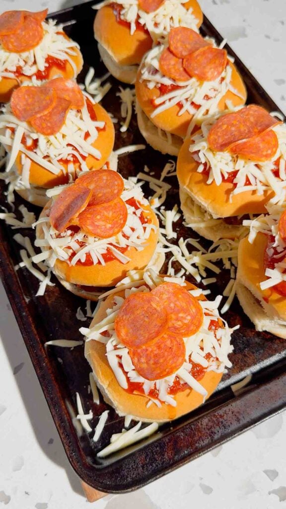 pepperoni and cheese topped burgers on a baking sheet
