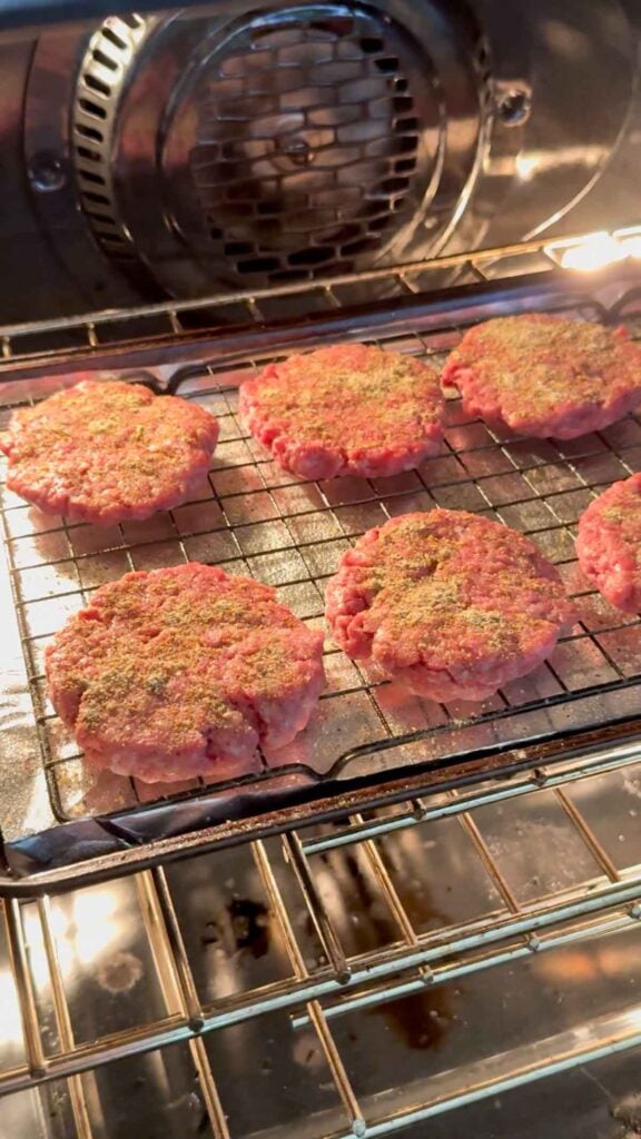 raw hamburger patties on a baking sheet in the oven