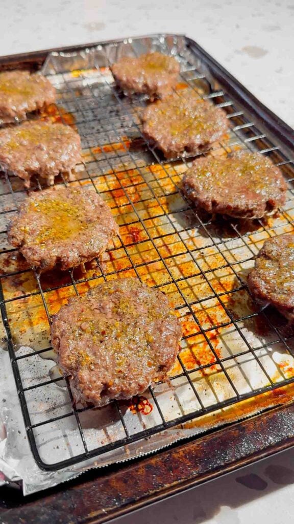 cooked hamburger patties on a rack on a foil lined baking sheet