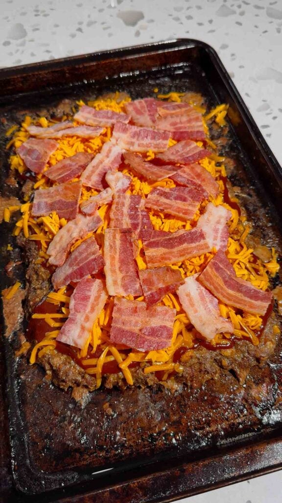 chopped bacon pieces on top of shreed cheddar and bbq sauce on meatloaf