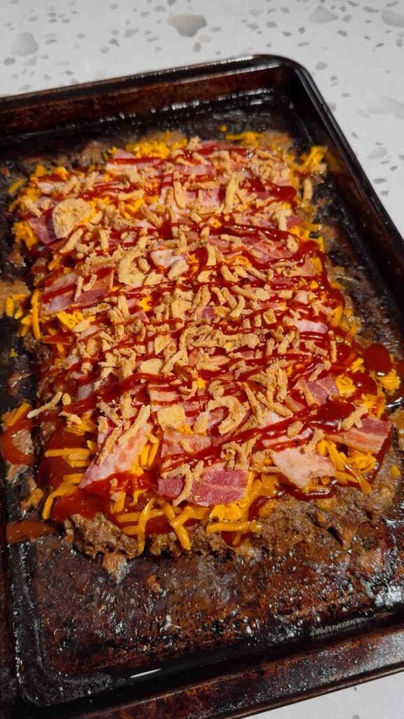 BBQ sauce drizzled over crispy fried onion and chopped bacon on top of cheeseburger meatloaf