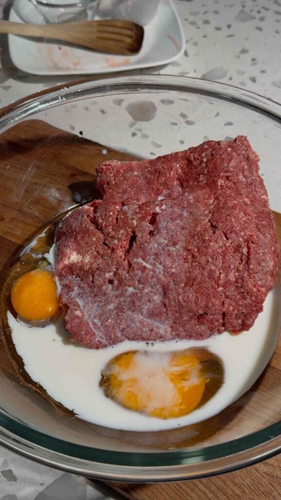 ground beef, eggs and milk in a glass bowl