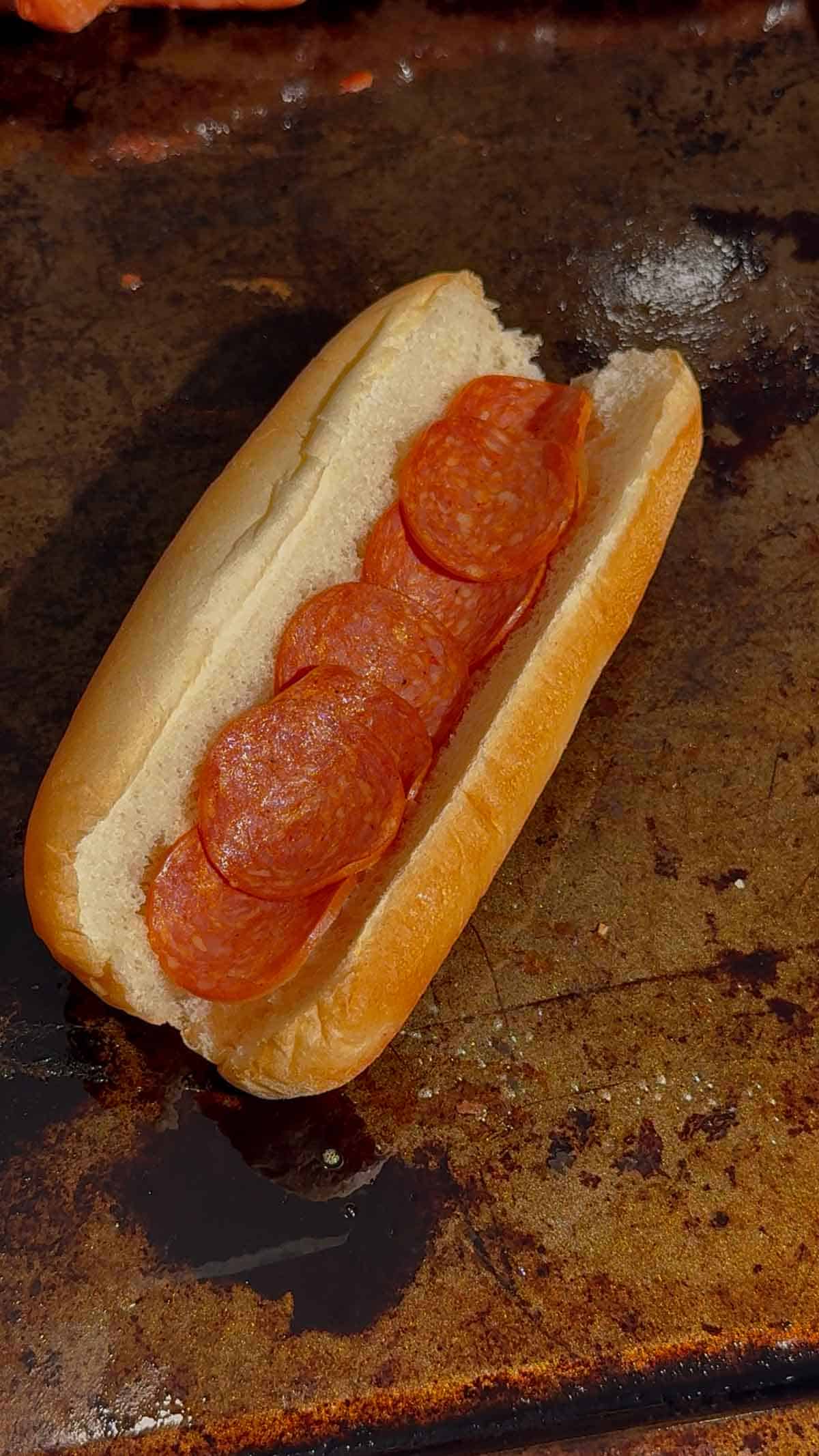 pepperoni slices in a hot dog bun on a baking sheet
