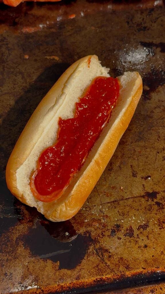 pizza sauce and pepperoni slices on a hot dog bun