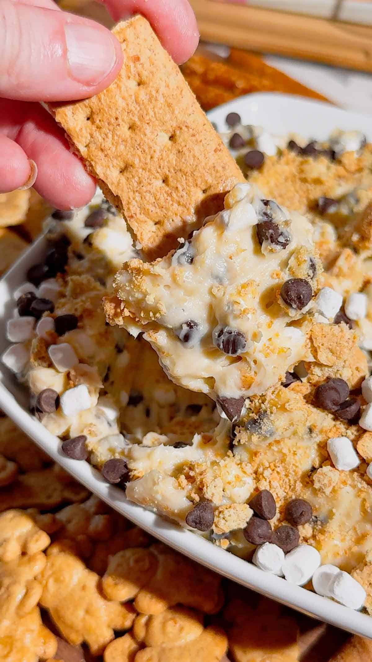 Looking for the ultimate S'mores Cookie Dough Dip to impress a crowd? This easy no bake dessert dip is rich, creamy, and loaded with mini chocolate chips, graham cracker crumbs, and marshmallows for that classic campfire flavor everyone loves. Perfect for Dessert Dips, No Bake Desserts, Easy Party Desserts, Cookie Dough Dip, S'mores Dessert Recipes, Summer Dessert Ideas, Sweet Dip Recipes, Holiday Dessert Ideas, Potluck Desserts, Game Day Desserts, Easy Dessert Recipes, and Fun Family Treats. Serve it with graham crackers, vanilla wafers, pretzels, strawberries, or apple slices for an irresistible dessert platter that's ready in only 10 minutes. Save this quick and easy dessert recipe for your next party, BBQ, movie night, or family gathering!