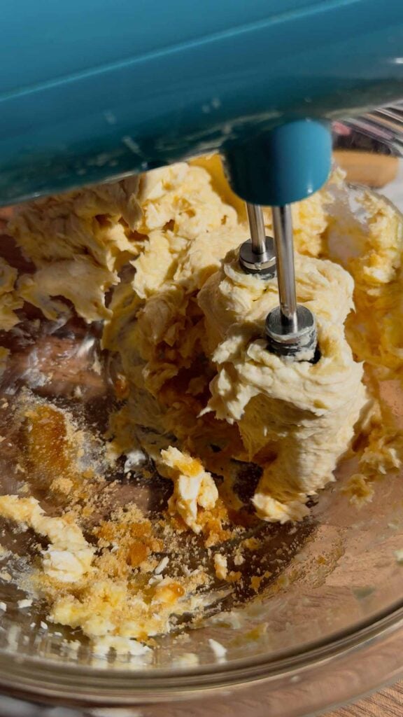 an electric mixer creaming together butter, cream cehese and sugar in a glass mixing bowl