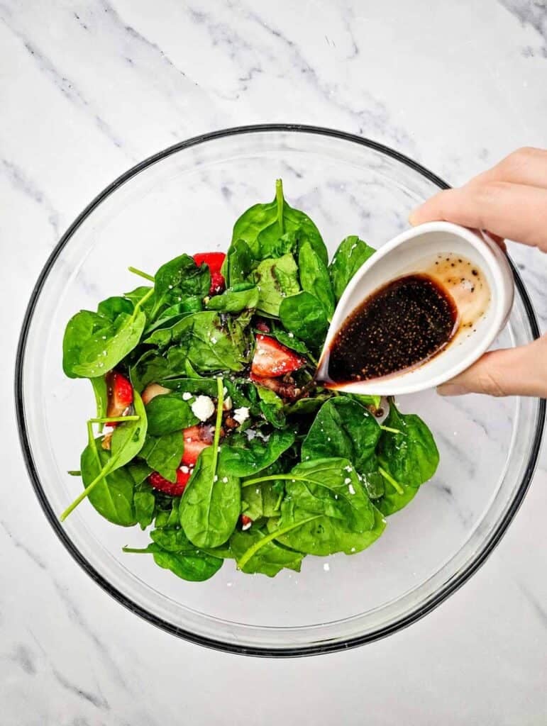 balsamic dressing being poured over strawberry spinach salad