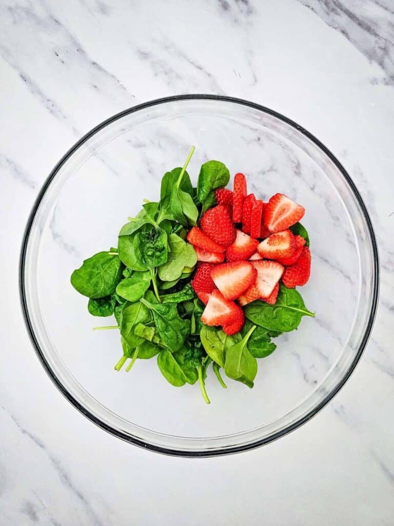 sliced strawberries and spinach in a glass mixing bowl