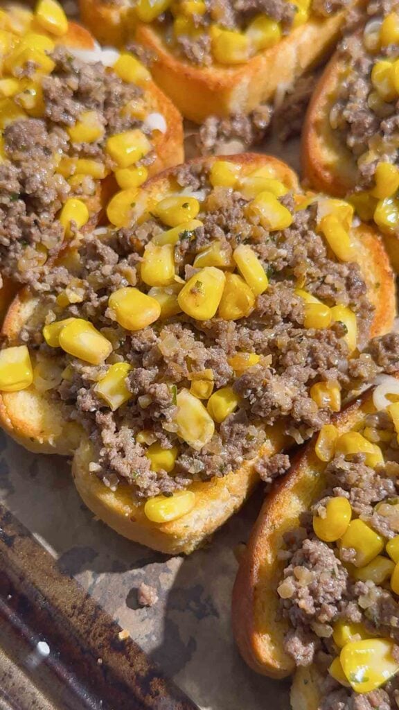 cooked ground beef and corn mixture on top of garlic toasts