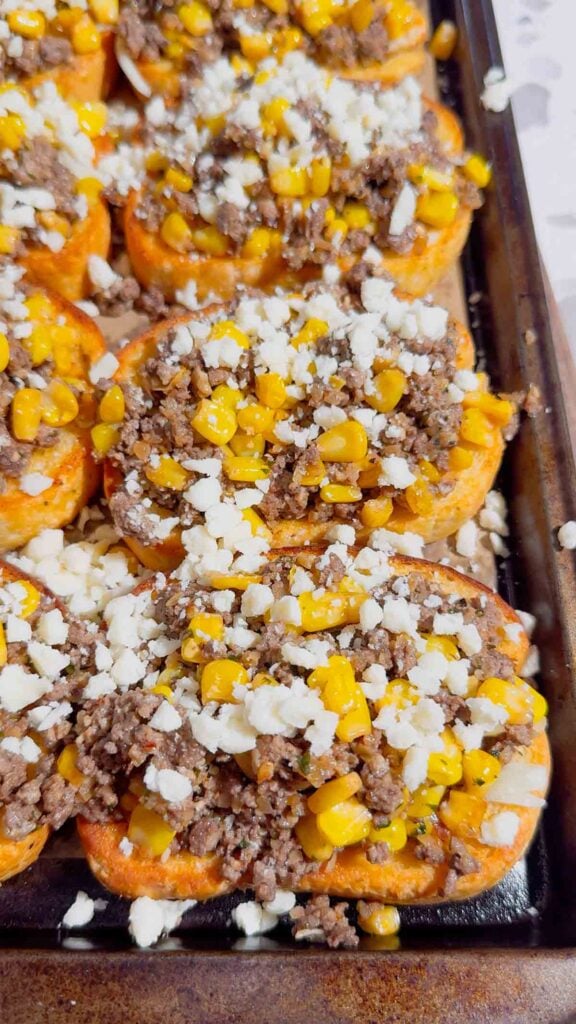 crumbled cotija cheese sprinkled on top of ground beef and corn mixture on garlic toasts