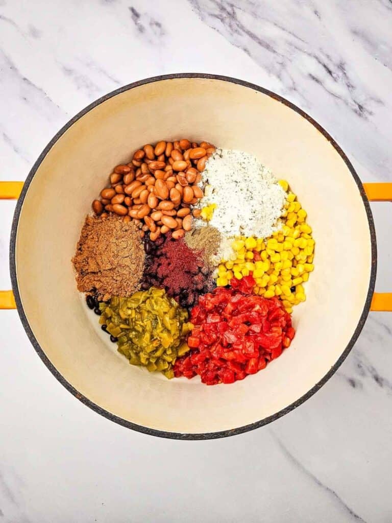seasonings on top of beans, corn and diced tomatoes in a large pot