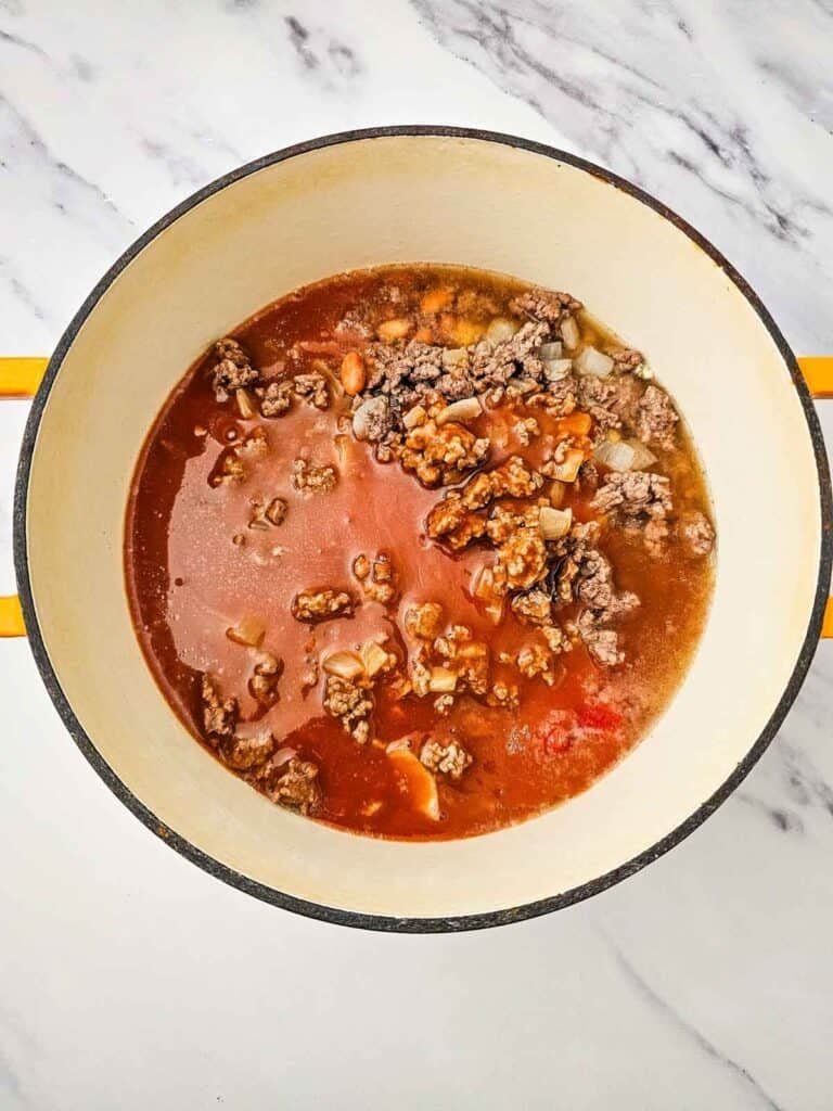 chicken broth and enchilada sauce added to large pot with veggies and cooked ground beef