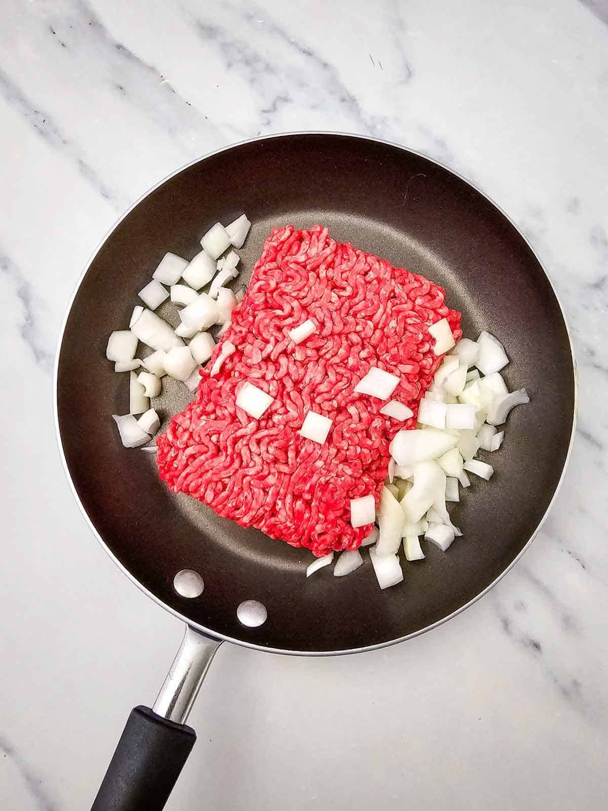 raw ground beef and diced onions in a skillet