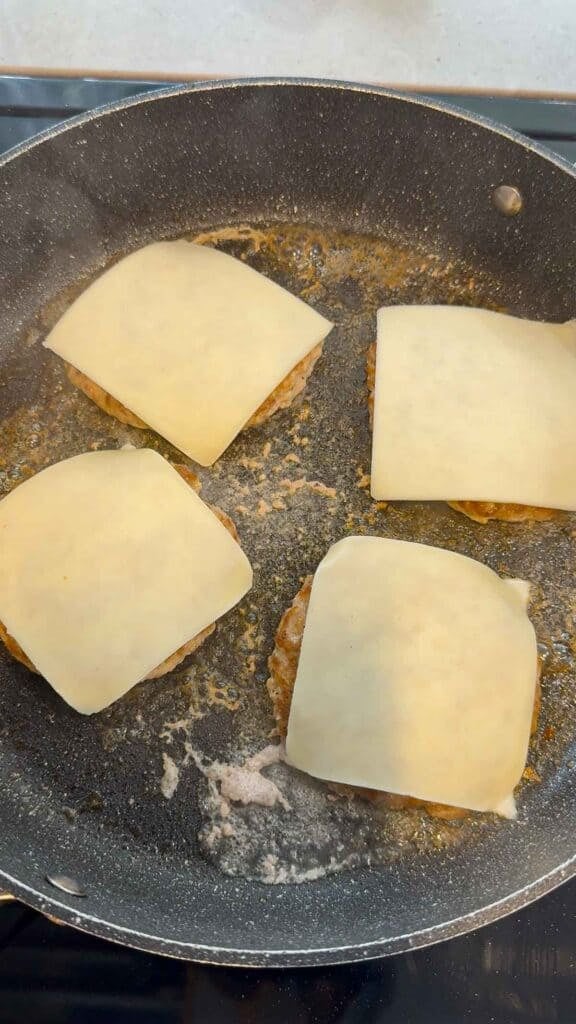 mozzarella cheese slices on top of chicken burger patties on a skillet