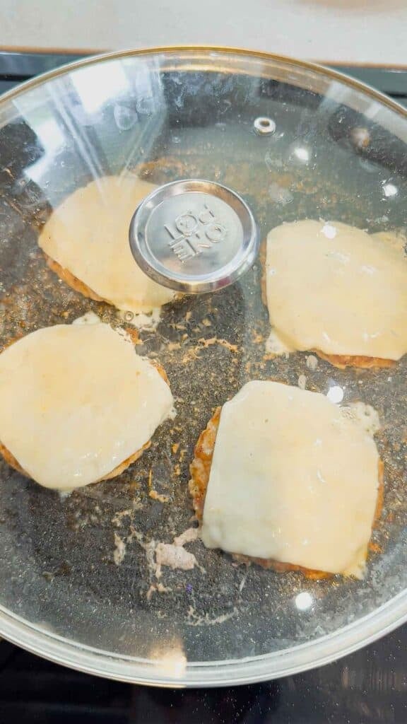 lid on skillet containing cheese topped chicken burger patties