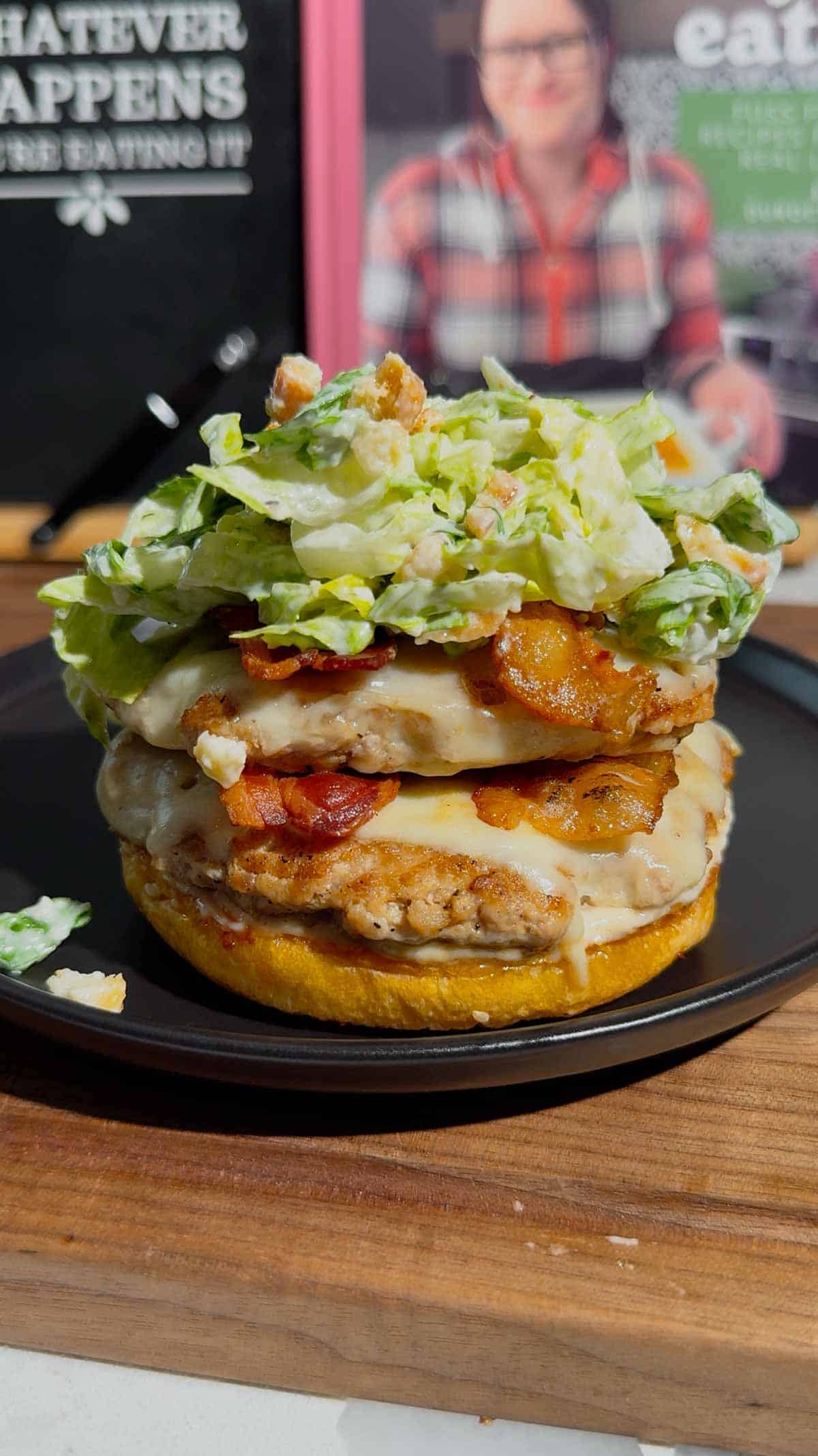 caesar salad on top of chicken patties and bacon slices on a burger bun