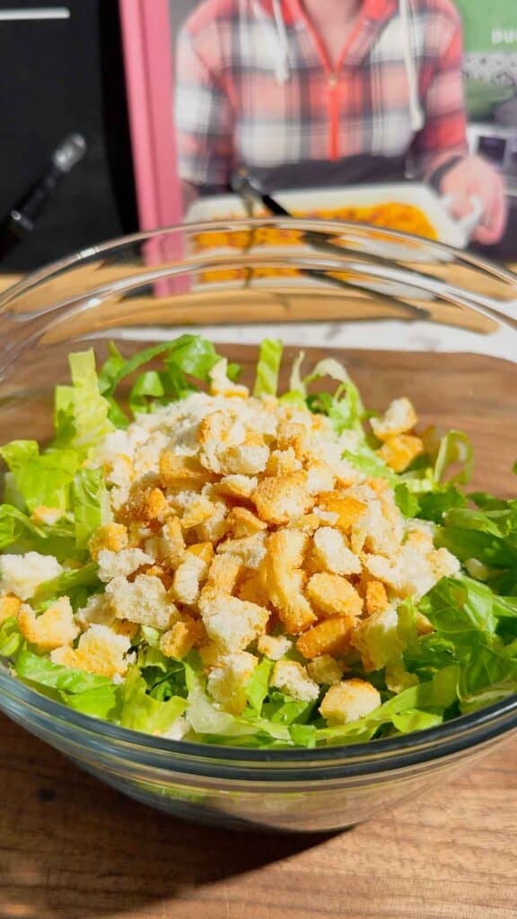 crumbled croutons, parmesan, caesar dressing and shredded romaine in a glass bowl
