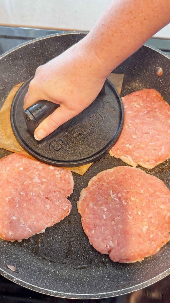 smashing chicken patties with a burger press in a skillet
