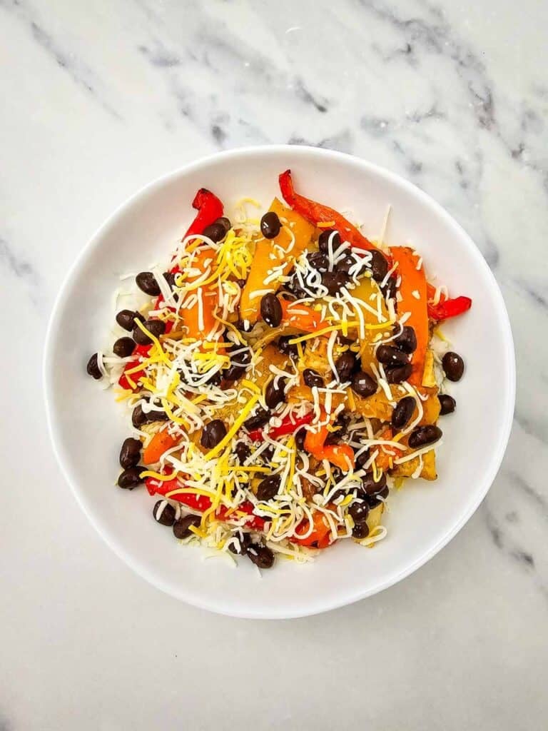 These easy Chicken Fajita Bowls are a flavorful weeknight dinner loaded with juicy seasoned chicken, colorful bell peppers, onions, fluffy rice, black beans, shredded cheese, and sour cream. If you love Chicken Fajita Bowl Recipes, Sheet Pan Chicken Fajitas, Mexican Chicken Bowls, or easy Chicken and Rice Bowls, this simple dinner is a must-try! The chicken and vegetables roast together on one sheet pan for easy prep and cleanup, then everything is piled into a delicious fajita rice bowl. Perfect for busy families, meal prep, quick dinners, and customizable meals everyone can top their own way. Save this Chicken Fajita Rice Bowl recipe when you need Easy Chicken Dinner Ideas, Mexican Dinner Recipes, Healthy Fajita Bowls, Sheet Pan Dinners, or quick family meals packed with bold fajita flavor!
