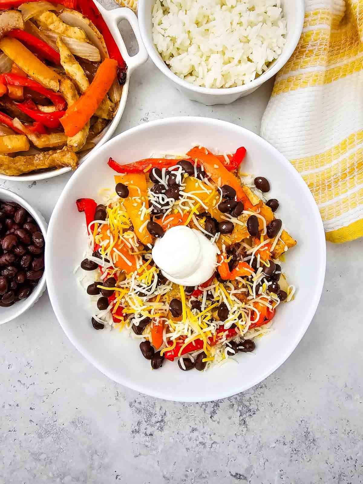 These easy Chicken Fajita Bowls are a flavorful weeknight dinner loaded with juicy seasoned chicken, colorful bell peppers, onions, fluffy rice, black beans, shredded cheese, and sour cream. If you love Chicken Fajita Bowl Recipes, Sheet Pan Chicken Fajitas, Mexican Chicken Bowls, or easy Chicken and Rice Bowls, this simple dinner is a must-try! The chicken and vegetables roast together on one sheet pan for easy prep and cleanup, then everything is piled into a delicious fajita rice bowl. Perfect for busy families, meal prep, quick dinners, and customizable meals everyone can top their own way. Save this Chicken Fajita Rice Bowl recipe when you need Easy Chicken Dinner Ideas, Mexican Dinner Recipes, Healthy Fajita Bowls, Sheet Pan Dinners, or quick family meals packed with bold fajita flavor!