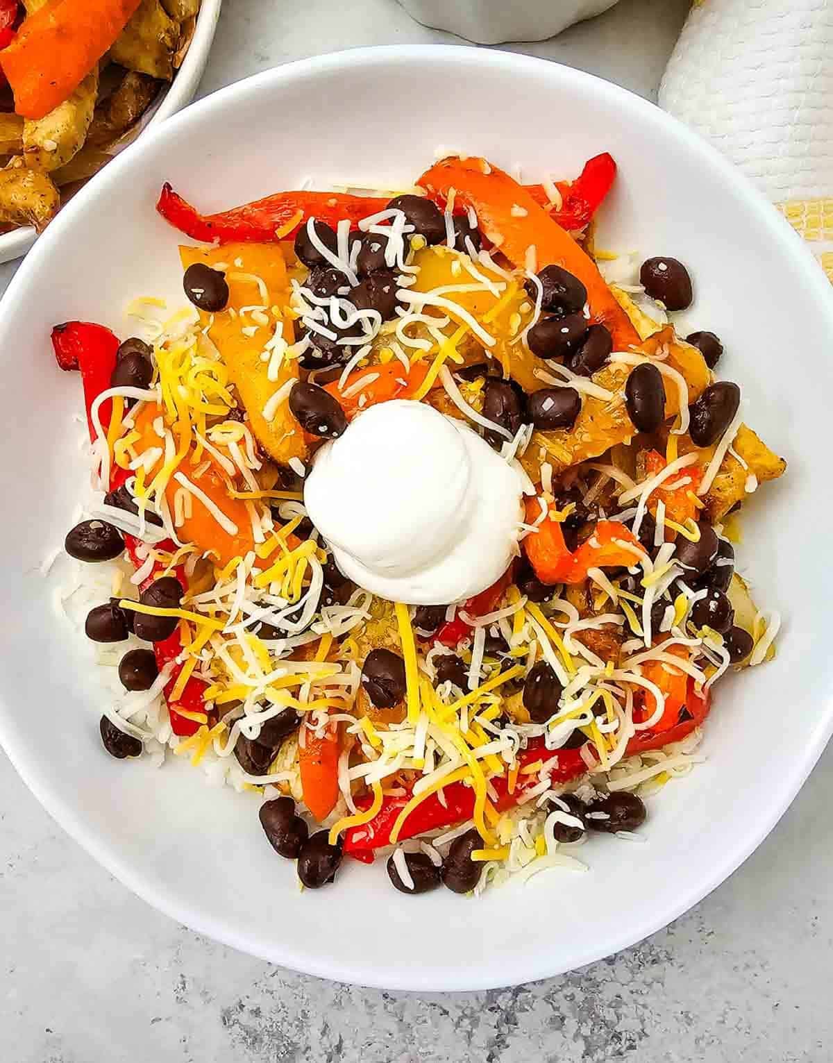 These easy Chicken Fajita Bowls are a flavorful weeknight dinner loaded with juicy seasoned chicken, colorful bell peppers, onions, fluffy rice, black beans, shredded cheese, and sour cream. If you love Chicken Fajita Bowl Recipes, Sheet Pan Chicken Fajitas, Mexican Chicken Bowls, or easy Chicken and Rice Bowls, this simple dinner is a must-try! The chicken and vegetables roast together on one sheet pan for easy prep and cleanup, then everything is piled into a delicious fajita rice bowl. Perfect for busy families, meal prep, quick dinners, and customizable meals everyone can top their own way. Save this Chicken Fajita Rice Bowl recipe when you need Easy Chicken Dinner Ideas, Mexican Dinner Recipes, Healthy Fajita Bowls, Sheet Pan Dinners, or quick family meals packed with bold fajita flavor!
