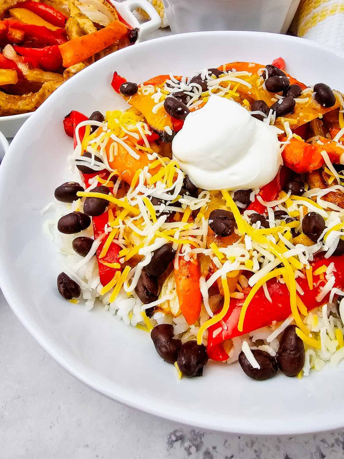 These easy Chicken Fajita Bowls are a flavorful weeknight dinner loaded with juicy seasoned chicken, colorful bell peppers, onions, fluffy rice, black beans, shredded cheese, and sour cream. If you love Chicken Fajita Bowl Recipes, Sheet Pan Chicken Fajitas, Mexican Chicken Bowls, or easy Chicken and Rice Bowls, this simple dinner is a must-try! The chicken and vegetables roast together on one sheet pan for easy prep and cleanup, then everything is piled into a delicious fajita rice bowl. Perfect for busy families, meal prep, quick dinners, and customizable meals everyone can top their own way. Save this Chicken Fajita Rice Bowl recipe when you need Easy Chicken Dinner Ideas, Mexican Dinner Recipes, Healthy Fajita Bowls, Sheet Pan Dinners, or quick family meals packed with bold fajita flavor!
