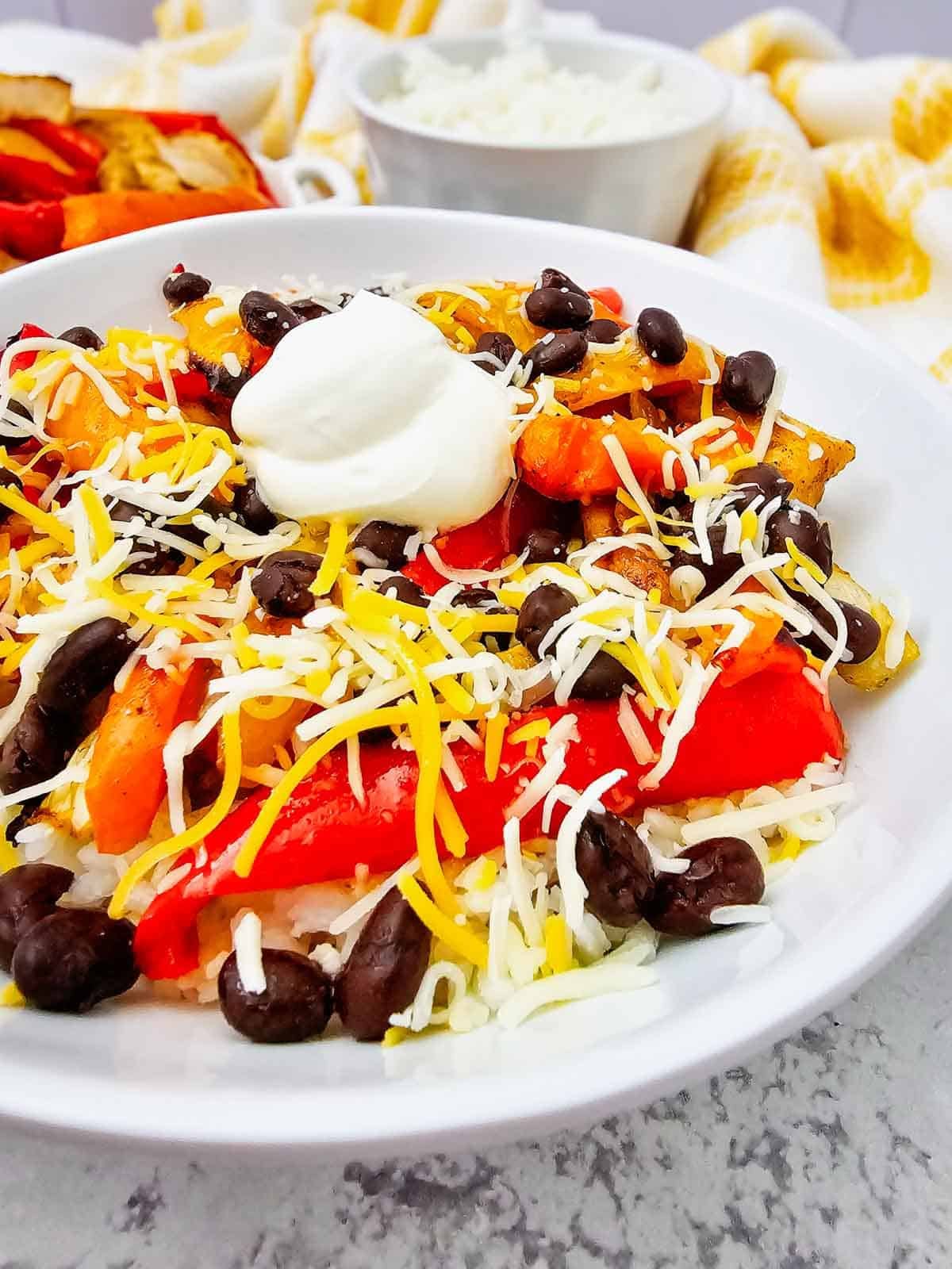 These easy Chicken Fajita Bowls are a flavorful weeknight dinner loaded with juicy seasoned chicken, colorful bell peppers, onions, fluffy rice, black beans, shredded cheese, and sour cream. If you love Chicken Fajita Bowl Recipes, Sheet Pan Chicken Fajitas, Mexican Chicken Bowls, or easy Chicken and Rice Bowls, this simple dinner is a must-try! The chicken and vegetables roast together on one sheet pan for easy prep and cleanup, then everything is piled into a delicious fajita rice bowl. Perfect for busy families, meal prep, quick dinners, and customizable meals everyone can top their own way. Save this Chicken Fajita Rice Bowl recipe when you need Easy Chicken Dinner Ideas, Mexican Dinner Recipes, Healthy Fajita Bowls, Sheet Pan Dinners, or quick family meals packed with bold fajita flavor!