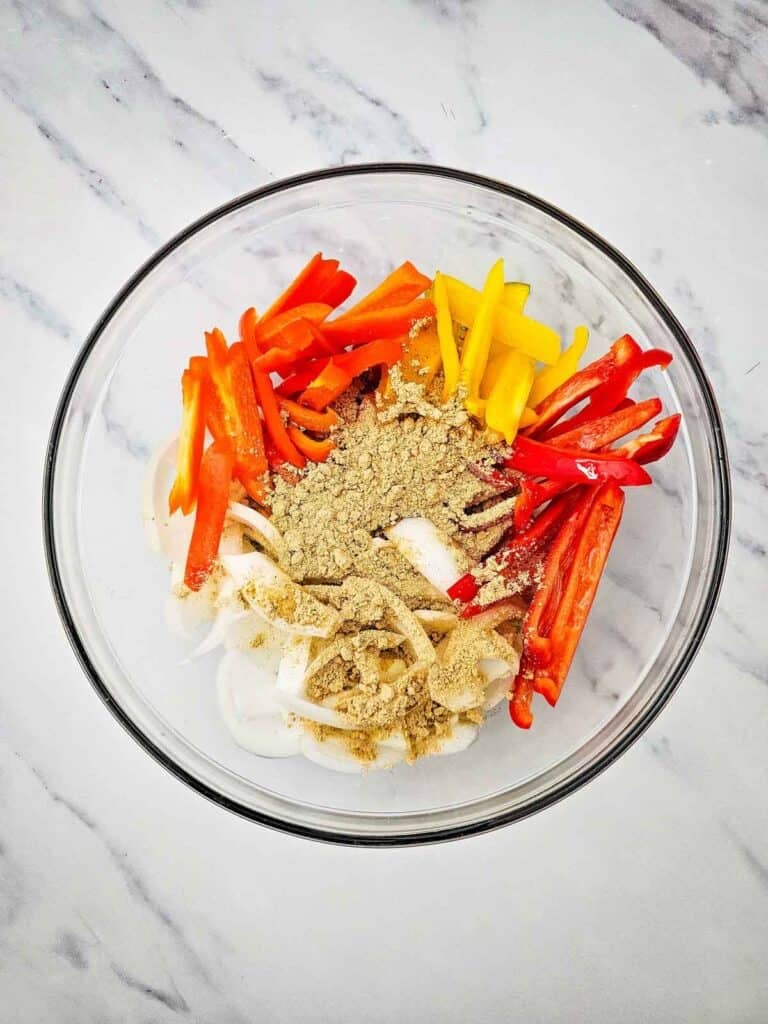 spices, sliced bell peppers and onions in a glass bowl