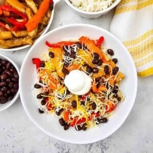 These easy Chicken Fajita Bowls are a flavorful weeknight dinner loaded with juicy seasoned chicken, colorful bell peppers, onions, fluffy rice, black beans, shredded cheese, and sour cream. If you love Chicken Fajita Bowl Recipes, Sheet Pan Chicken Fajitas, Mexican Chicken Bowls, or easy Chicken and Rice Bowls, this simple dinner is a must-try! The chicken and vegetables roast together on one sheet pan for easy prep and cleanup, then everything is piled into a delicious fajita rice bowl. Perfect for busy families, meal prep, quick dinners, and customizable meals everyone can top their own way. Save this Chicken Fajita Rice Bowl recipe when you need Easy Chicken Dinner Ideas, Mexican Dinner Recipes, Healthy Fajita Bowls, Sheet Pan Dinners, or quick family meals packed with bold fajita flavor!