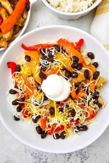 These easy Chicken Fajita Bowls are a flavorful weeknight dinner loaded with juicy seasoned chicken, colorful bell peppers, onions, fluffy rice, black beans, shredded cheese, and sour cream. If you love Chicken Fajita Bowl Recipes, Sheet Pan Chicken Fajitas, Mexican Chicken Bowls, or easy Chicken and Rice Bowls, this simple dinner is a must-try! The chicken and vegetables roast together on one sheet pan for easy prep and cleanup, then everything is piled into a delicious fajita rice bowl. Perfect for busy families, meal prep, quick dinners, and customizable meals everyone can top their own way. Save this Chicken Fajita Rice Bowl recipe when you need Easy Chicken Dinner Ideas, Mexican Dinner Recipes, Healthy Fajita Bowls, Sheet Pan Dinners, or quick family meals packed with bold fajita flavor!