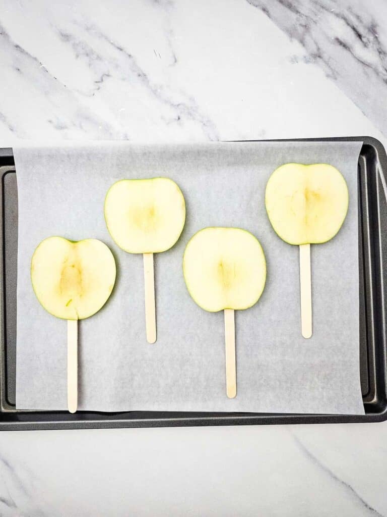 apple slices on sticks on a parchment lined baking sheet