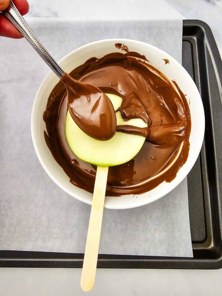 coating an apple slice on a stick in chocolate