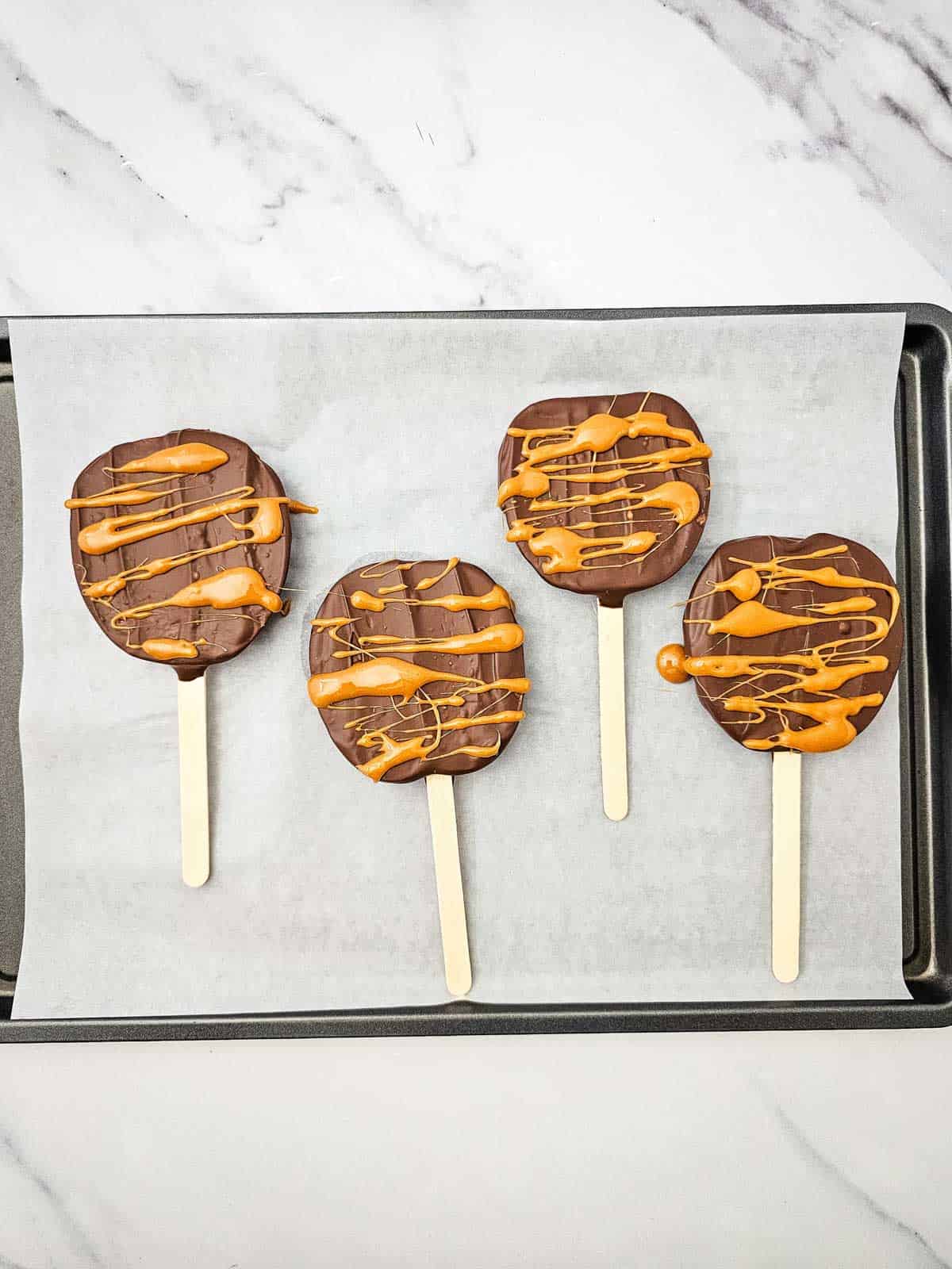 caramel and chocolate coated apple slices on a parchment lined baking sheet