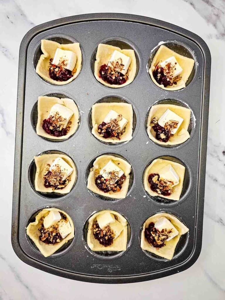 puff pastry in muffin tins filled with brie, cranberry sauce and pecans