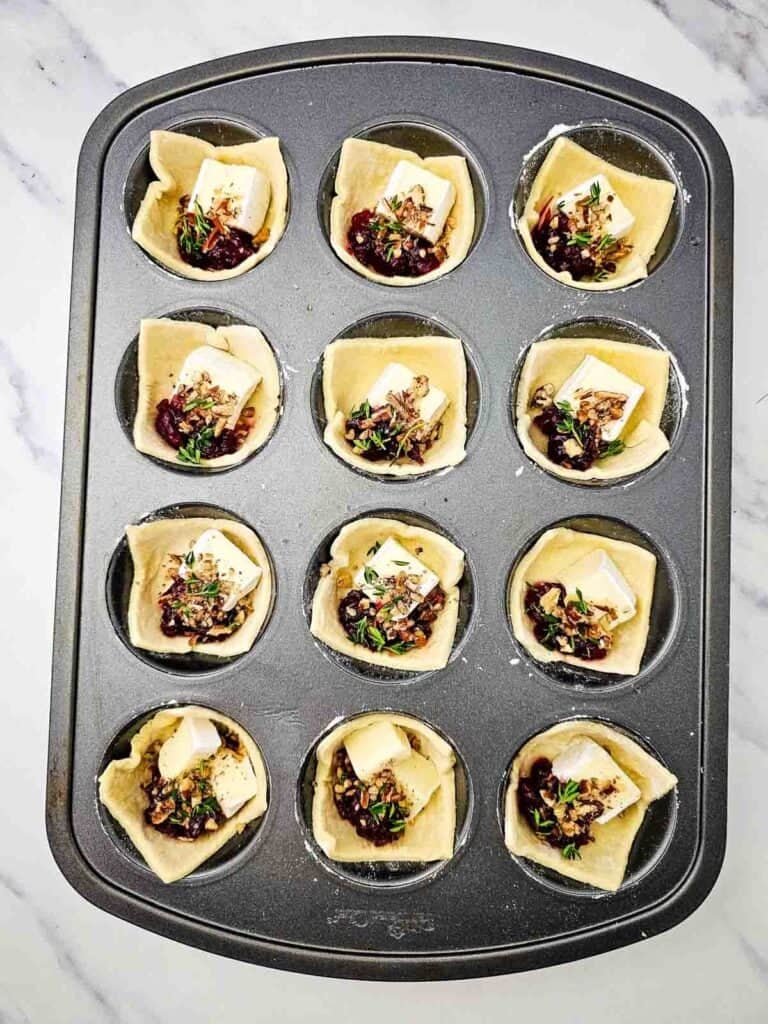 puff pastry in muffin tins filled with brie, cranberry sauce, pecans and thyme