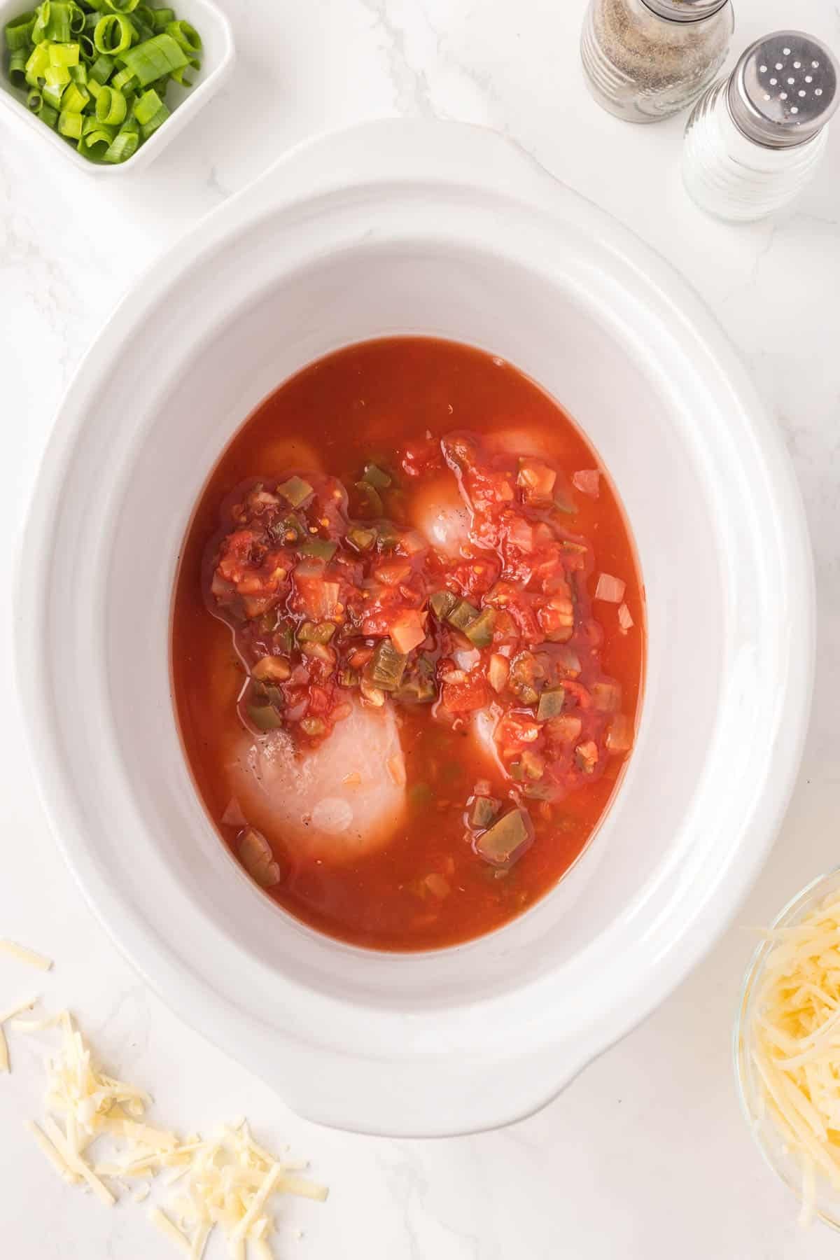 salsa poured over chicken breasts in a crock pot