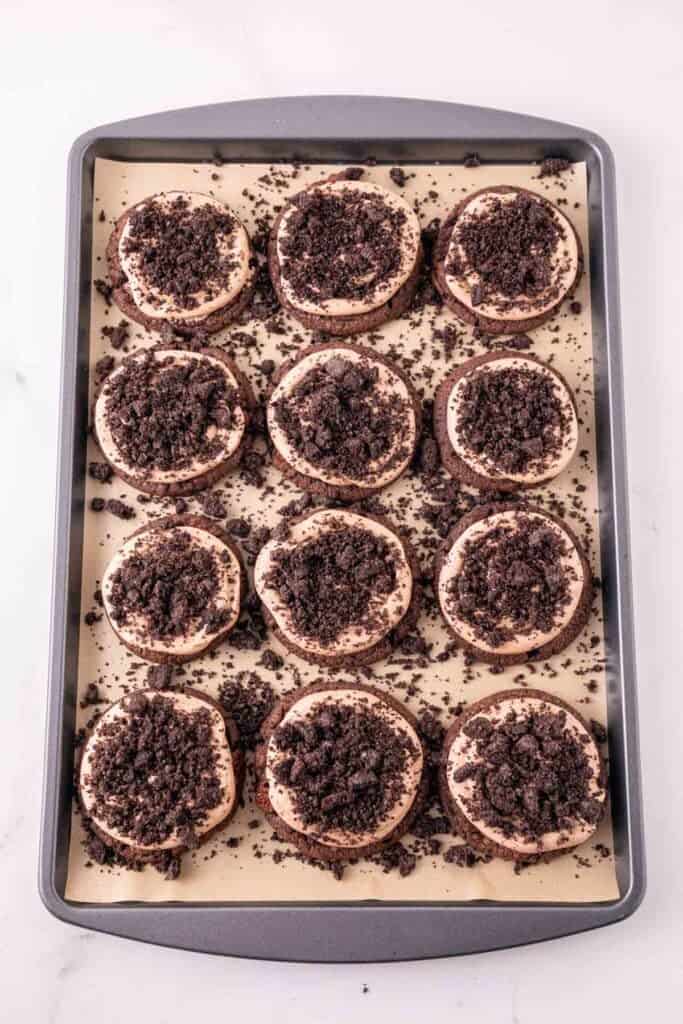 oreo crumbs on top of nutella frosted chocolate cooikies on a baking sheet